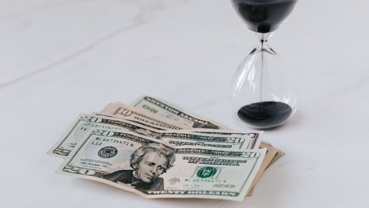 From above of transparent glass with black sand on white table and pile of paper money with image of president