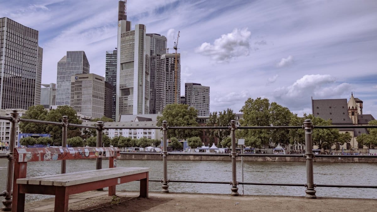 Urban view of Frankfurt skyline and Main River with a park bench in foreground.