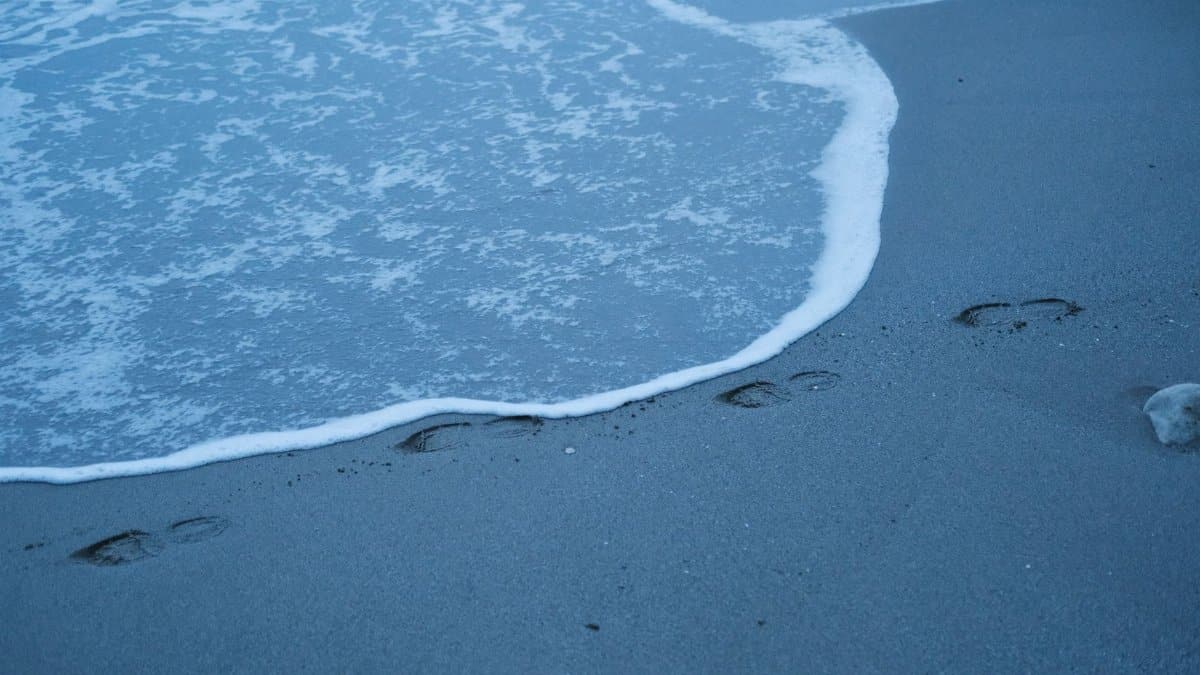 Serene ocean waves wash over sandy footprints on a quiet beach shoreline.