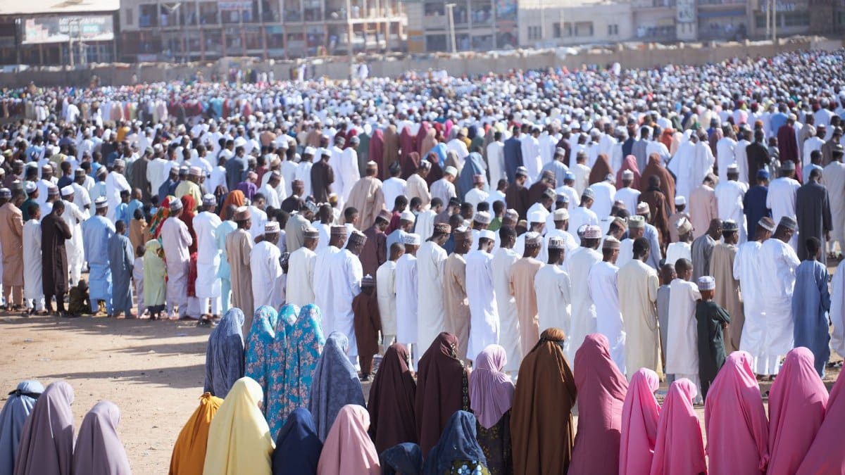 A vast crowd gathers for communal prayer outdoors showing vibrant cultural attire.