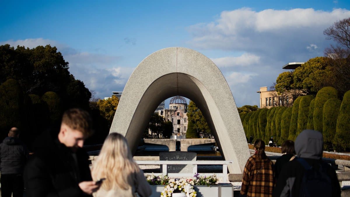 Visitors at Hiroshima Peace Memorial Park with cenotaph arch framing the Atomic Bomb Dome in the background.