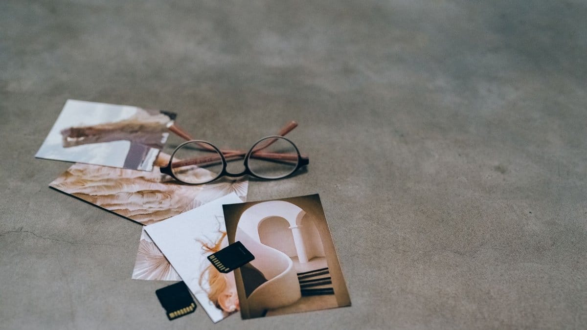 A creative flat lay of eyeglasses, printed photos, and memory cards on a concrete surface.