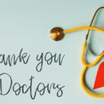 From above arrangement of yellow stethoscope with red heart shape placed on blue background with THANK YOU DOCTORS inscription