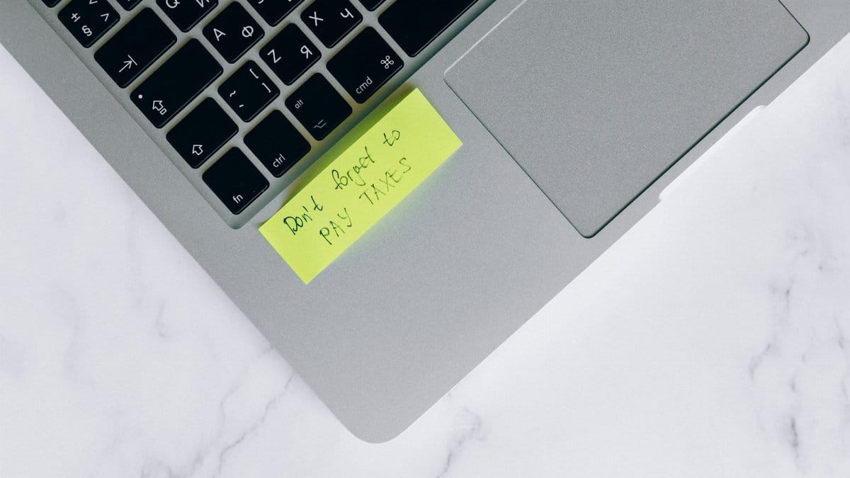 Close-up of a sticky note on a laptop reminding to pay taxes, emphasizing tax season.
