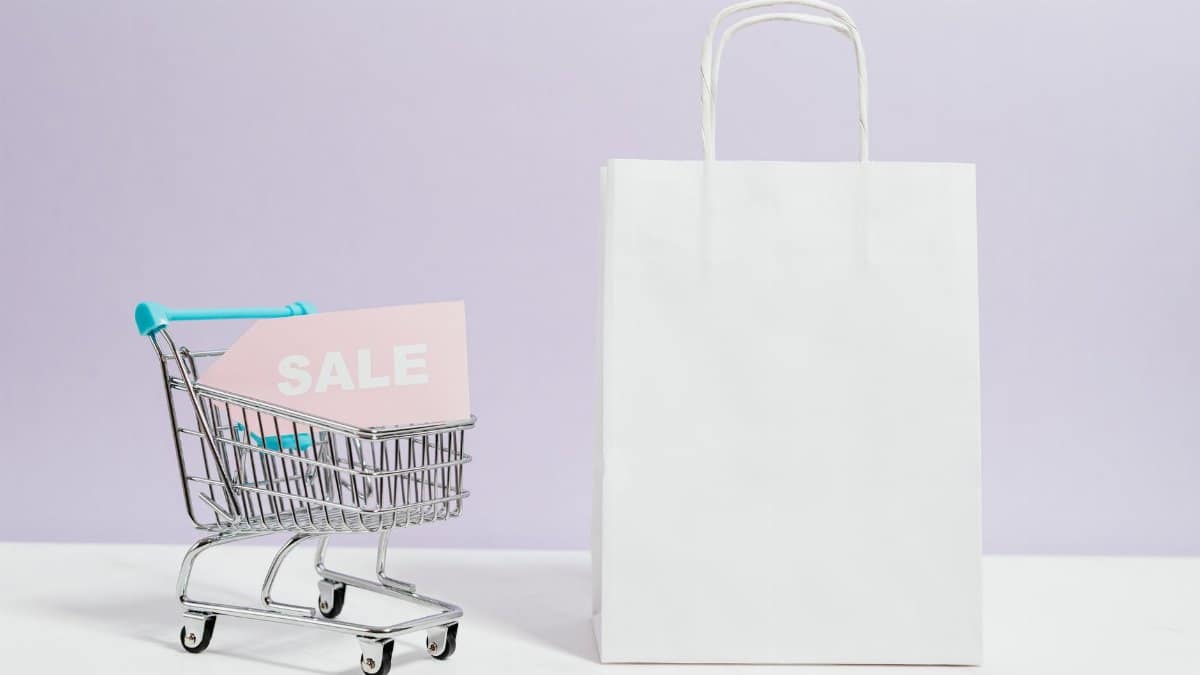 A miniature shopping cart with a sale sign beside a paper bag, perfect for online shopping themes.