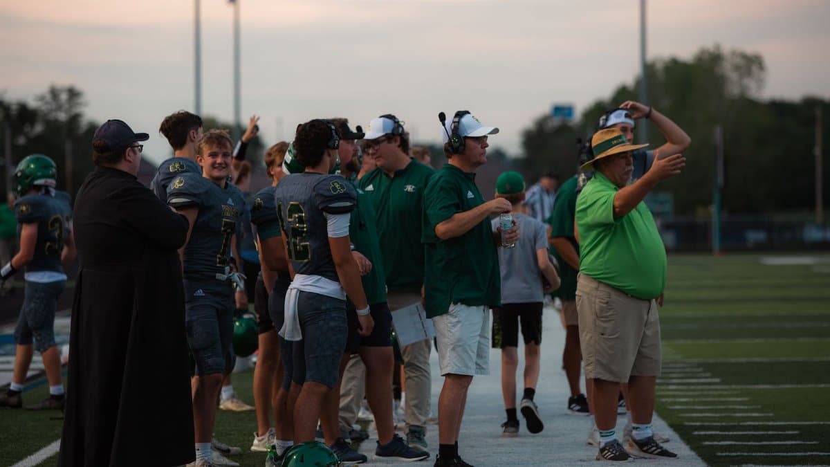 Coaches and players on high school football sidelines during a game.