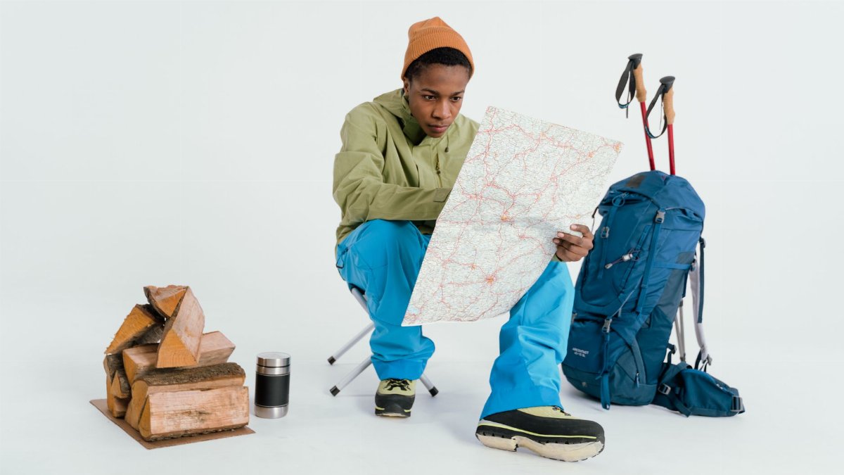 Black man preparing for winter hiking adventure with map and gear setup.