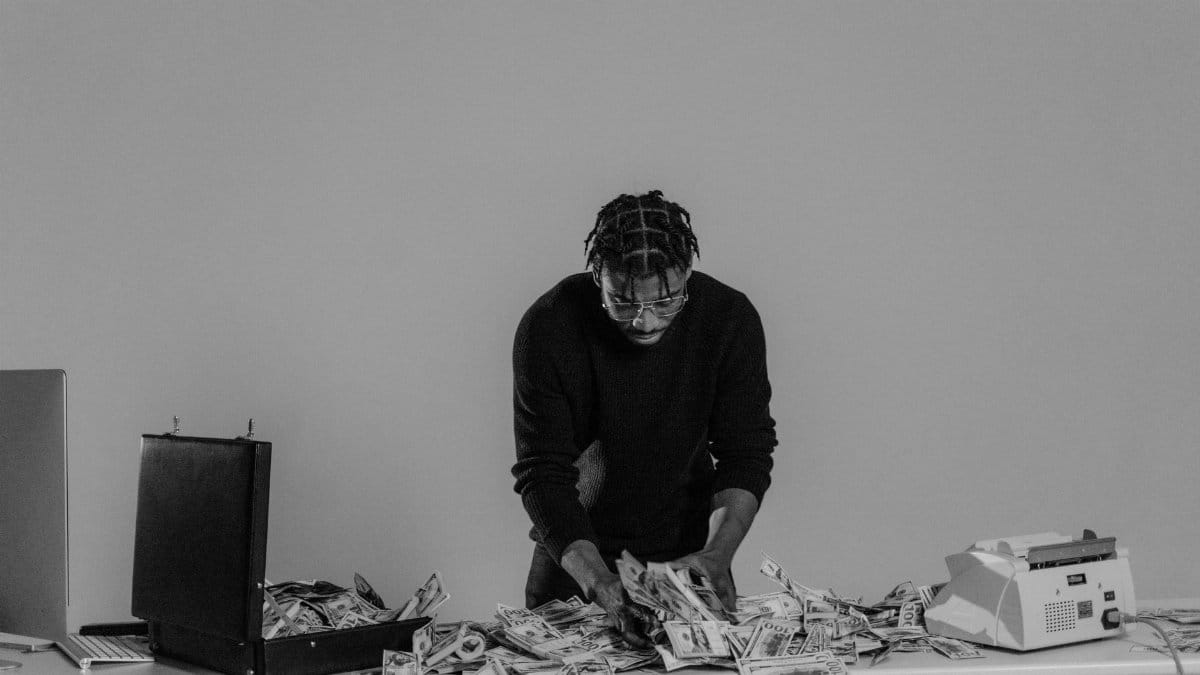 Black and white photo of a man sorting cash on a table with a briefcase.