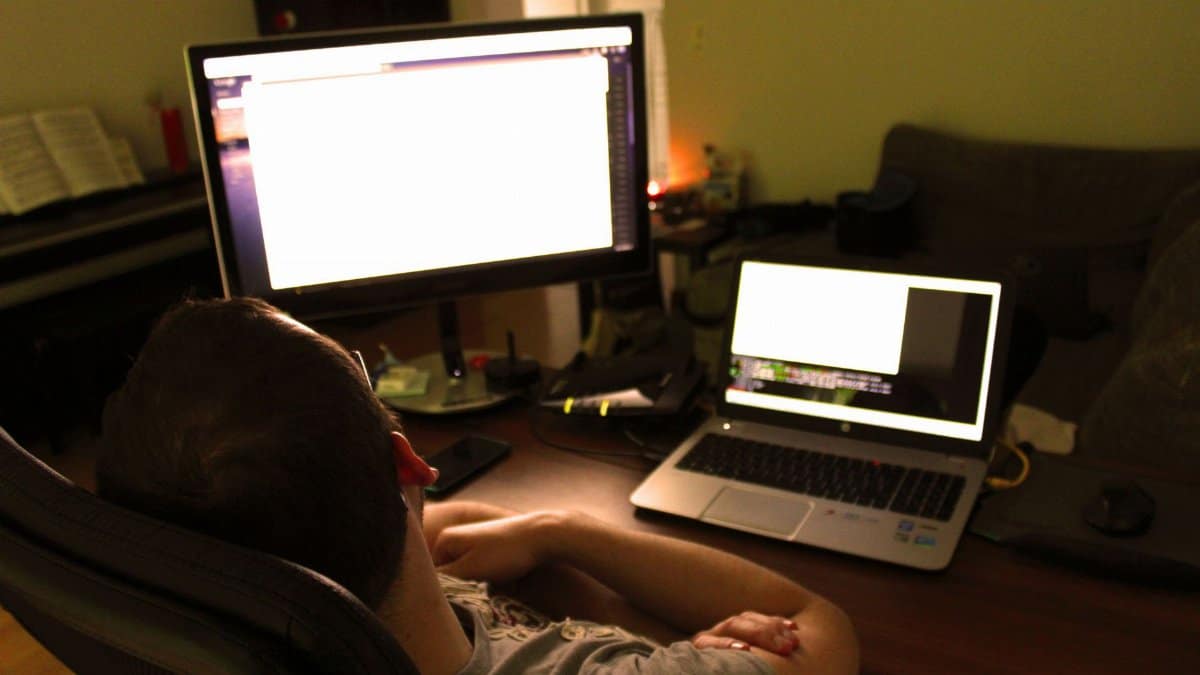 A man sitting at a desk working on a laptop and desktop, embodying modern remote work setup.