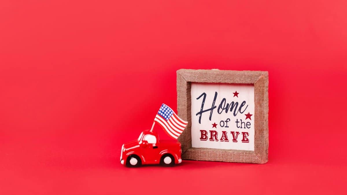 A miniature car with an American flag and 'Home of the Brave' sign on a red background.