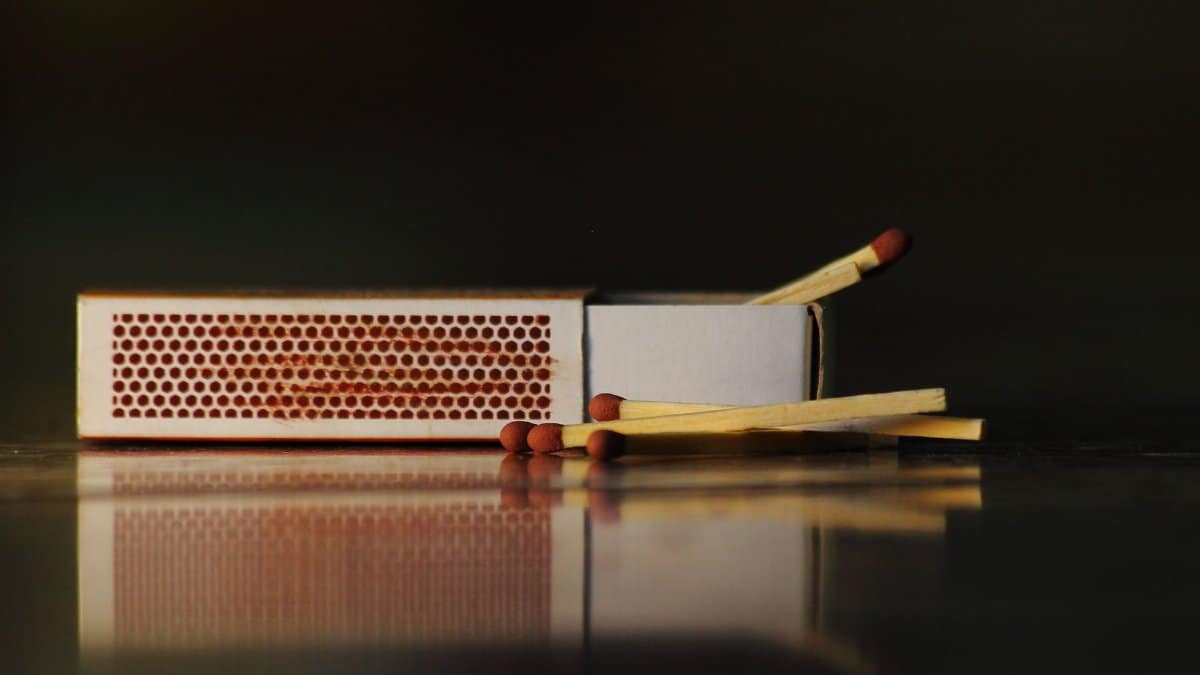 A still life photo of an open matchbox with wooden matches on a reflective surface.