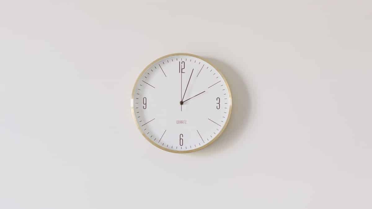 Minimalist round wall clock with gold rim and white face on a white wall.