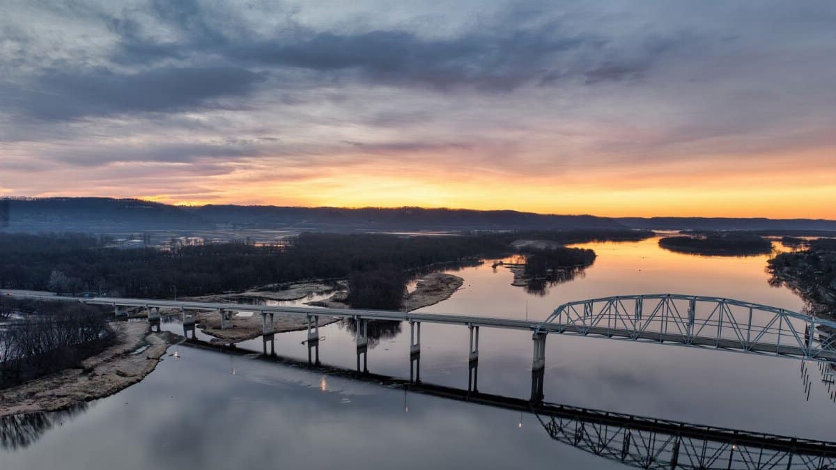 An aerial view of a bridge over the Mississippi River at sunrise in Wabasha, Minnesota, capturing tranquil reflections and vibrant colors.