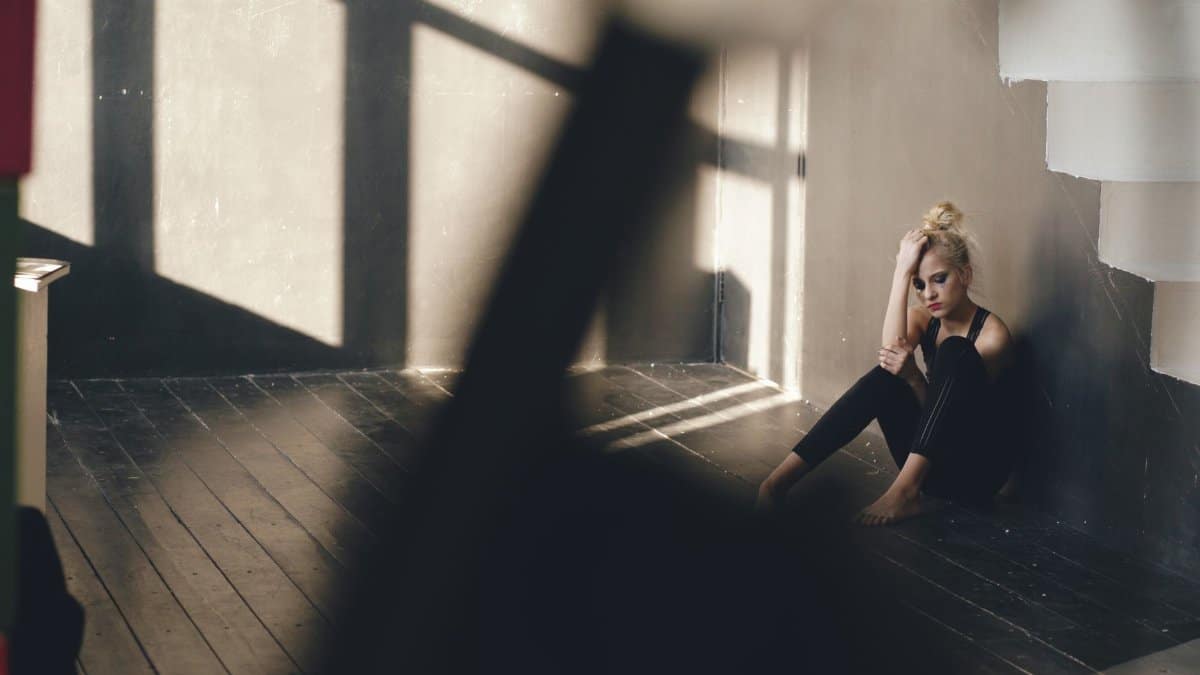 Woman sitting alone in a corner of a sunlit room, reflecting sadness and solitude.