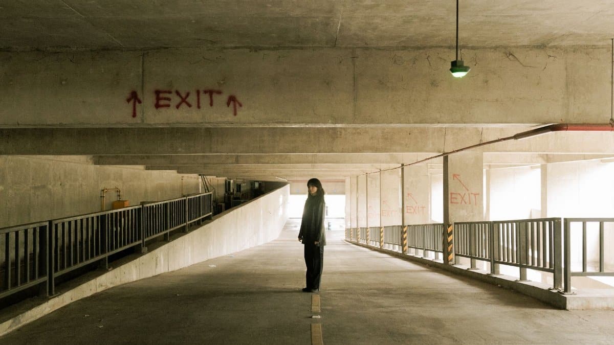 Individual in a quiet, dimly lit parking structure with exit sign.