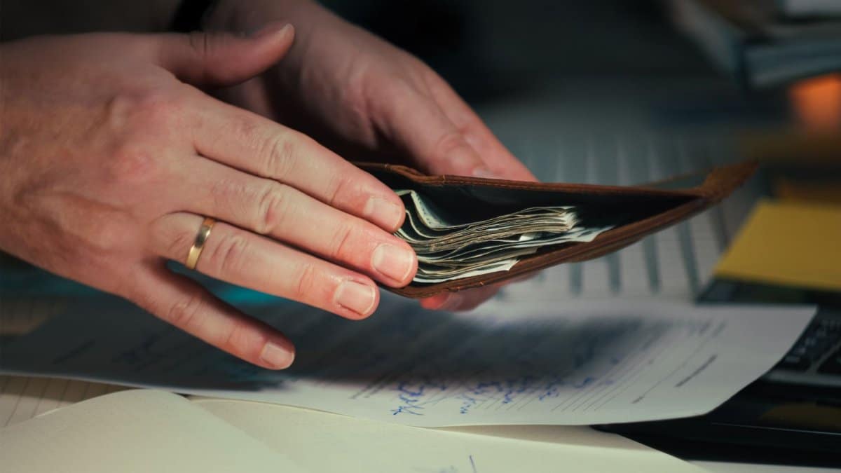 Hands holding an open wallet filled with cash above documents, indicating financial planning or budgeting.