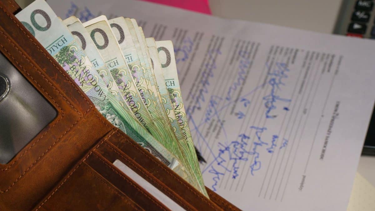 Close-up of a wallet containing Polish Zloty with a signed document in the background, representing financial transactions.