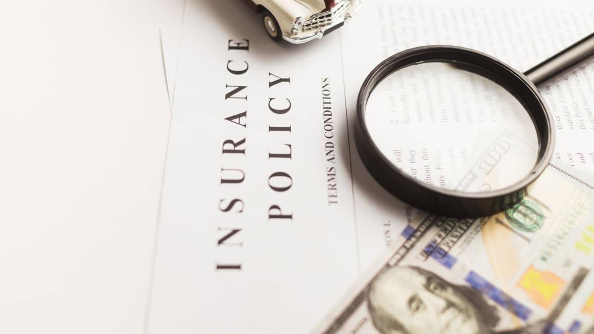 Close-up image of an insurance policy with a magnifying glass, money, and toy car.