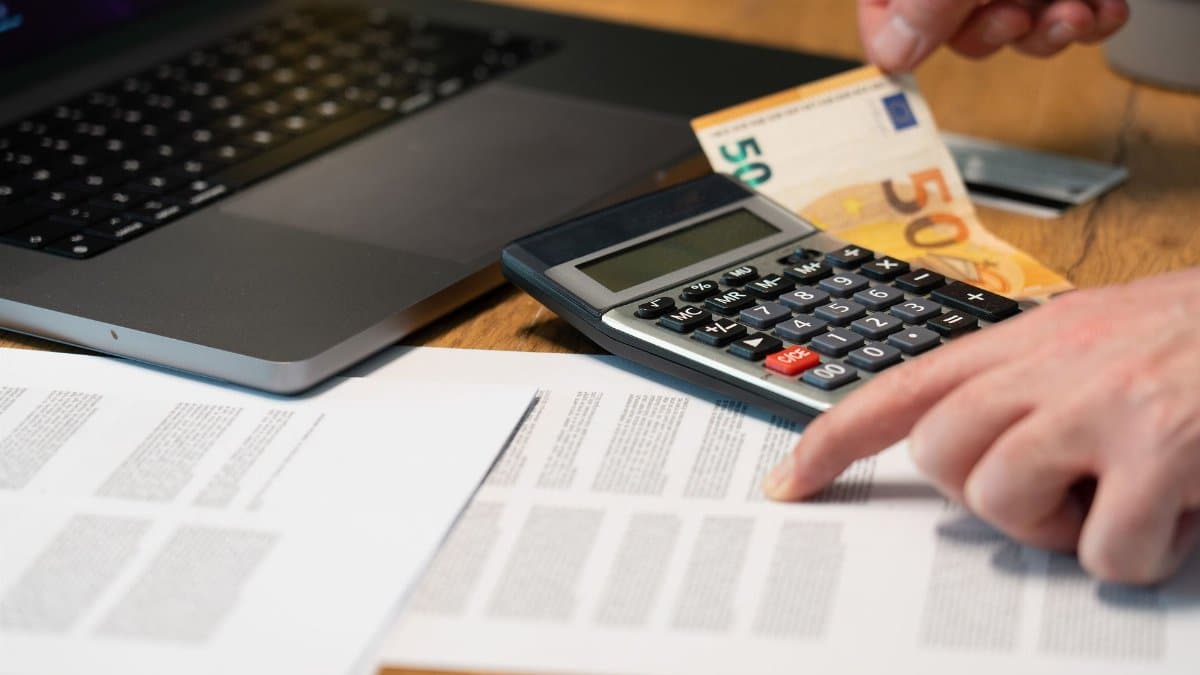Close-up of hands using calculator with euro notes and laptop on desk.