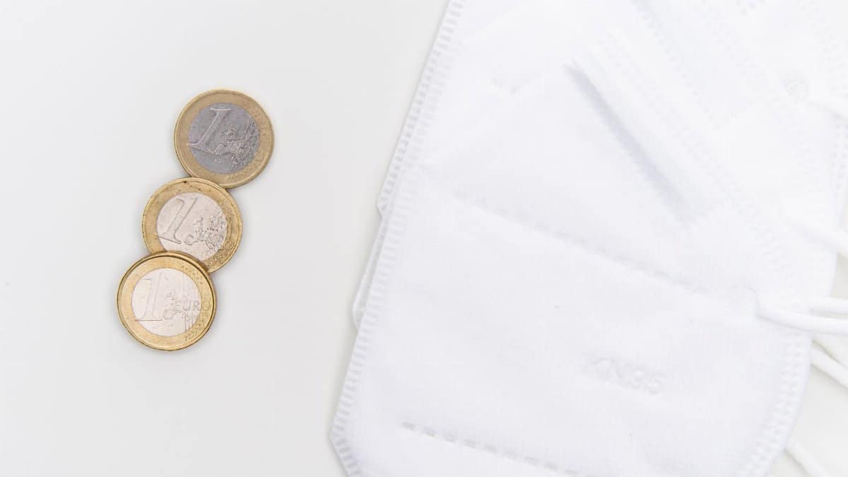 Euro coins alongside KN95 masks on a white surface, symbolizing safety and cost.