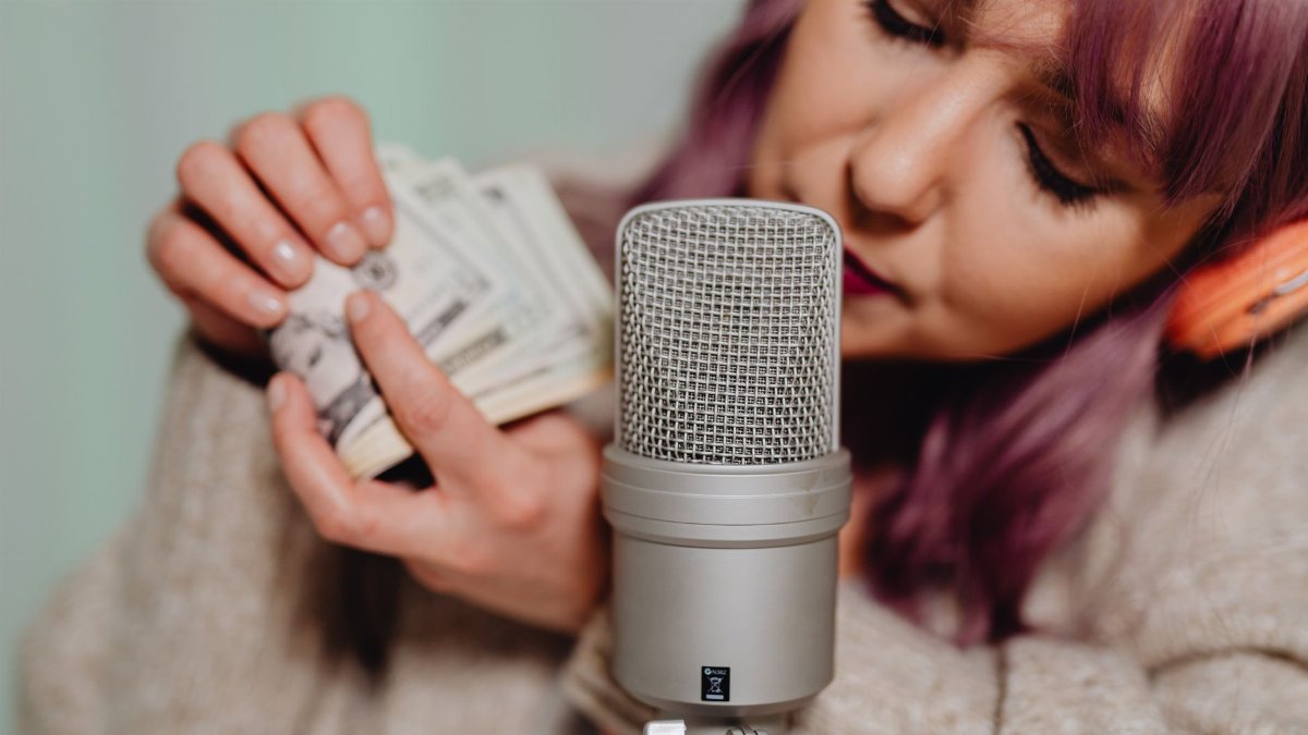 A young woman uses a microphone and money for an ASMR video indoors.