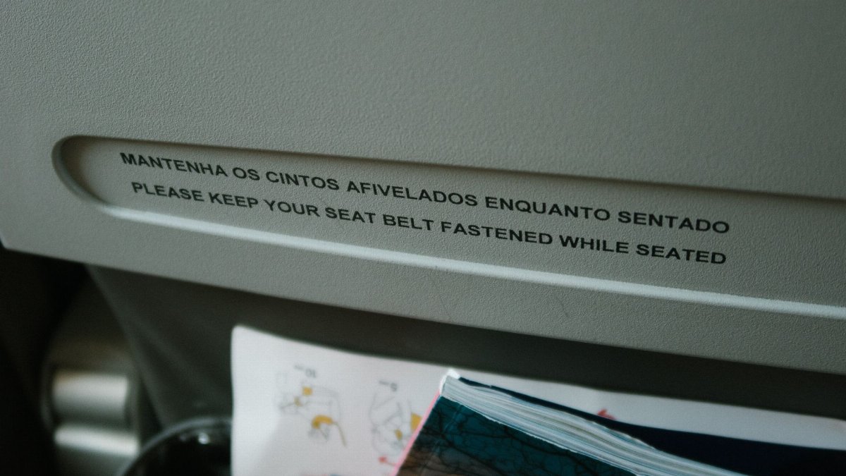 Close-up of an airplane seatback pocket with a seat belt safety message in English and Portuguese.
