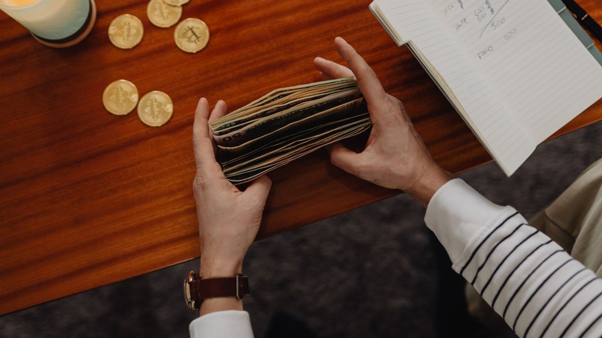 Close-up of a person organizing money with cryptocurrency coins on a wooden table, symbolizing modern finance.