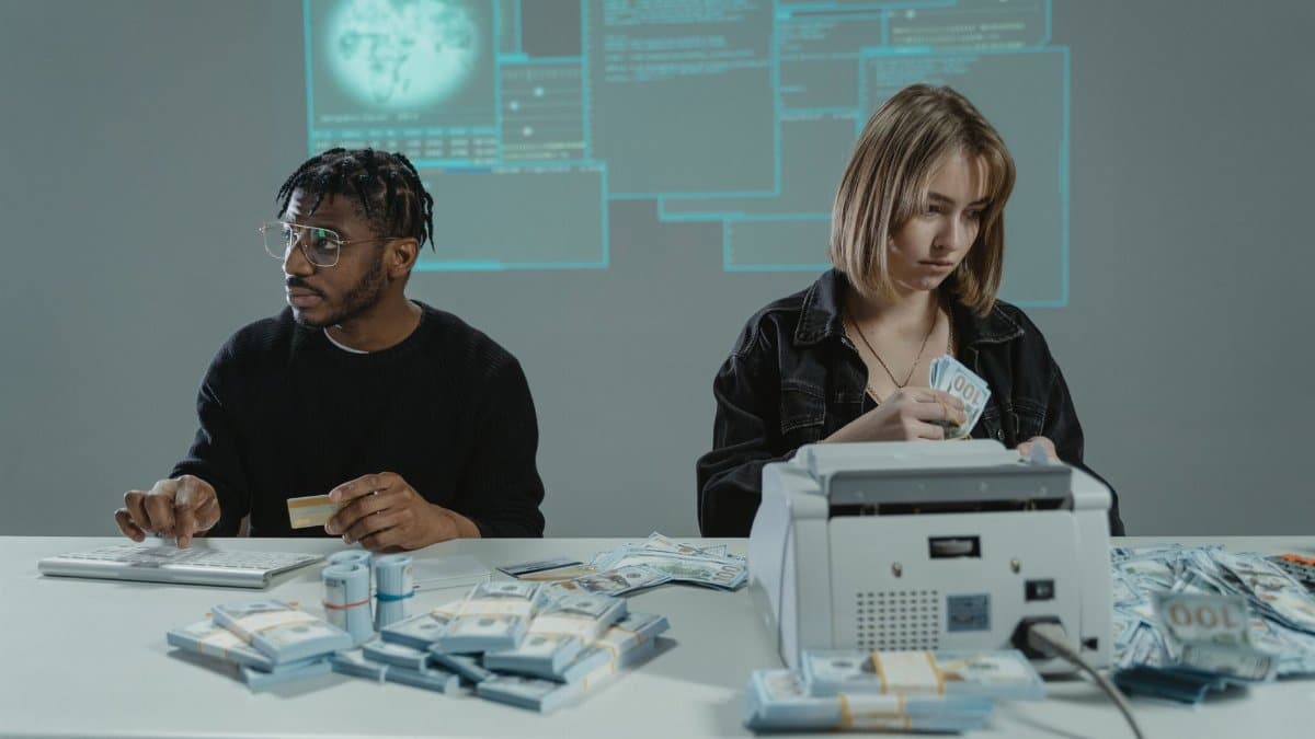Two individuals counting US dollar bills with a money machine, highlighting finance themes.