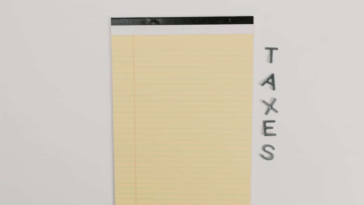 Close-up of a yellow legal pad and the word 'TAXES' on a white surface, ideal for finance themes.