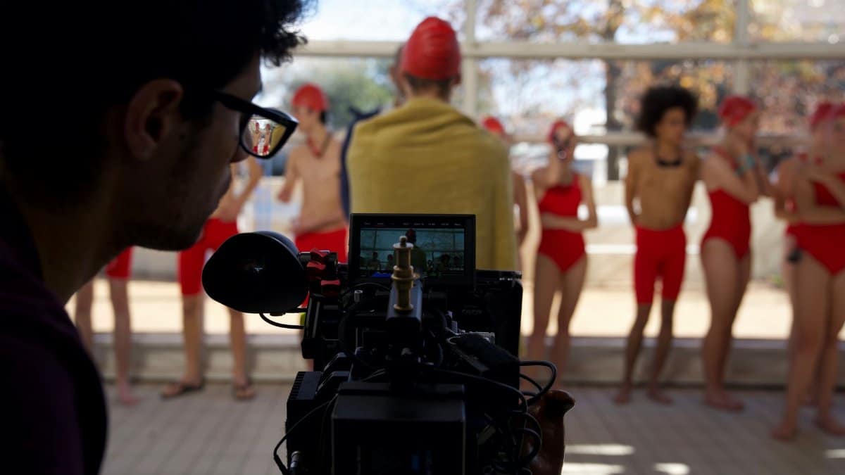 Behind-the-scenes view of a cameraman recording a swim team indoors.