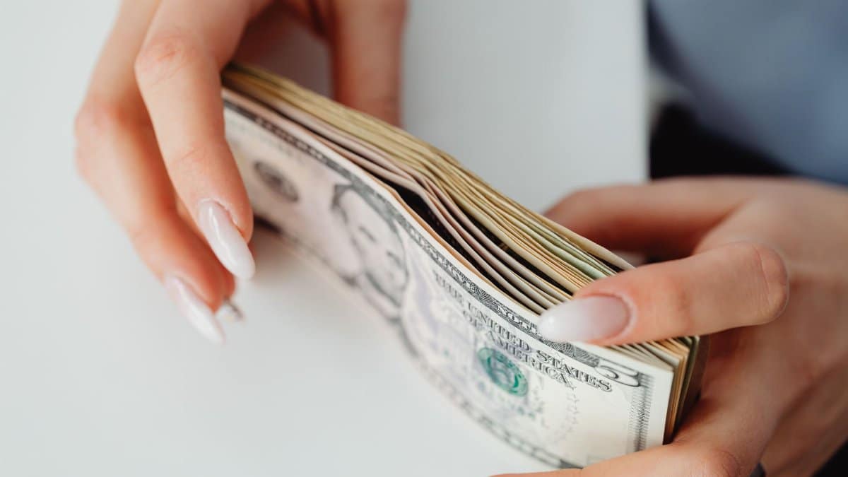 Hands carefully holding a stack of US dollar bills, representing finance and currency.