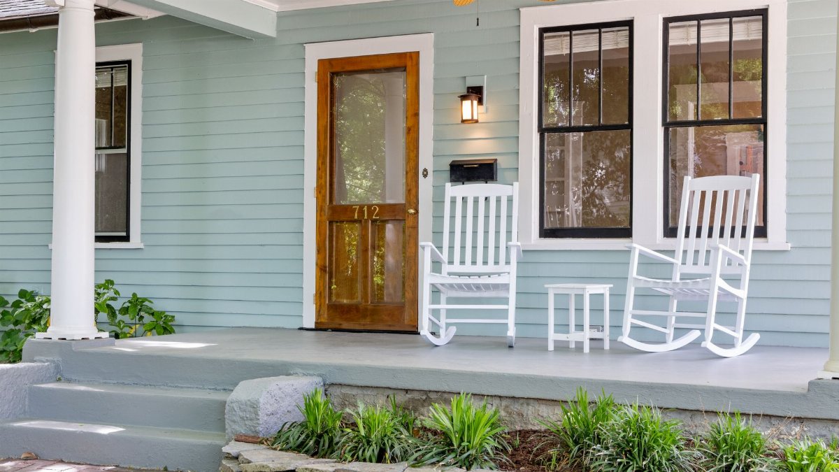 Inviting front porch featuring white rocking chairs and a wooden door, perfect for relaxation.