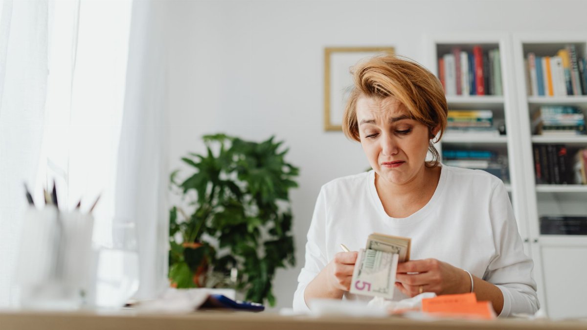A woman concernedly counts money at her desk in a bright room.