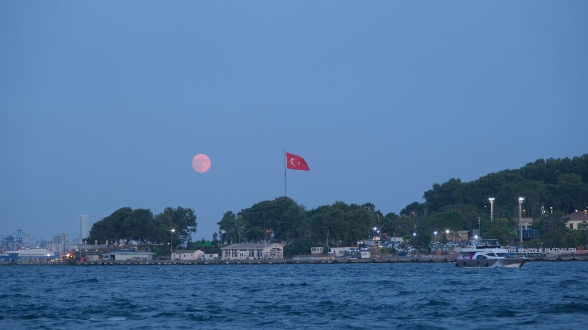 Dusk scene of Istanbul waterfront with a full moon and Turkish flag, showcasing the city's stunning skyline.