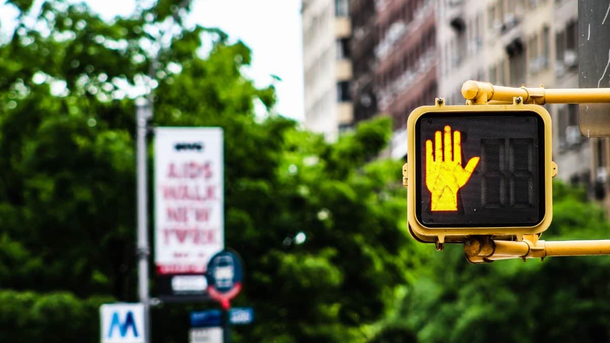 A vibrant New York City street scene featuring a pedestrian stop signal with lush greenery and buildings in the background.