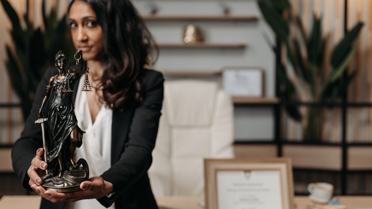 A female lawyer presenting a Lady Justice statue in a modern office setting.
