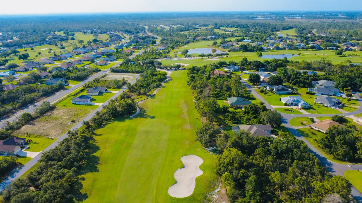Beautiful aerial view of a suburban golf course with lush greenery and homes in the distance.