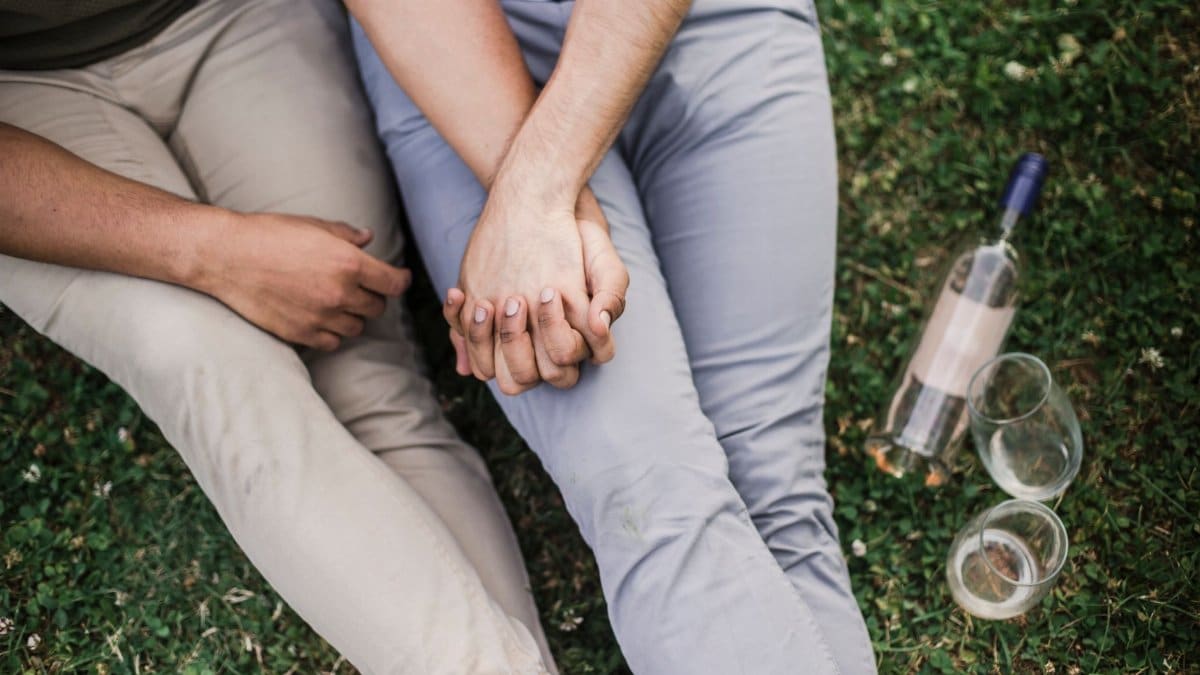 Interracial couple enjoying a romantic moment on grass with wine.