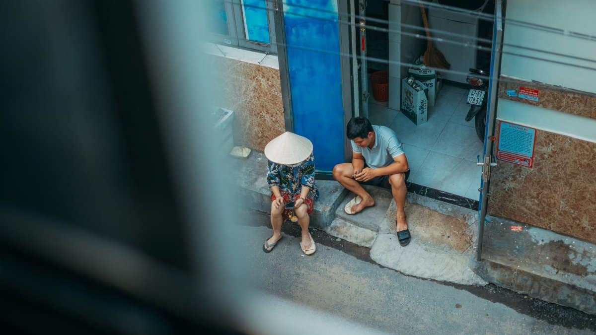 High angle view of two men sitting near a doorway in an urban setting, one wearing a conical hat.
