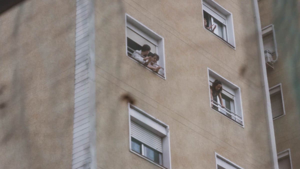 People looking out from windows in a city apartment building showing urban life.