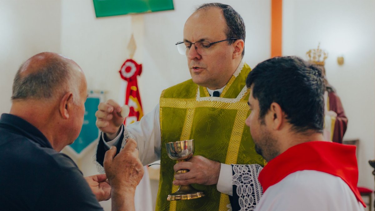 A priest administering Holy Communion to men during a religious service inside a church.