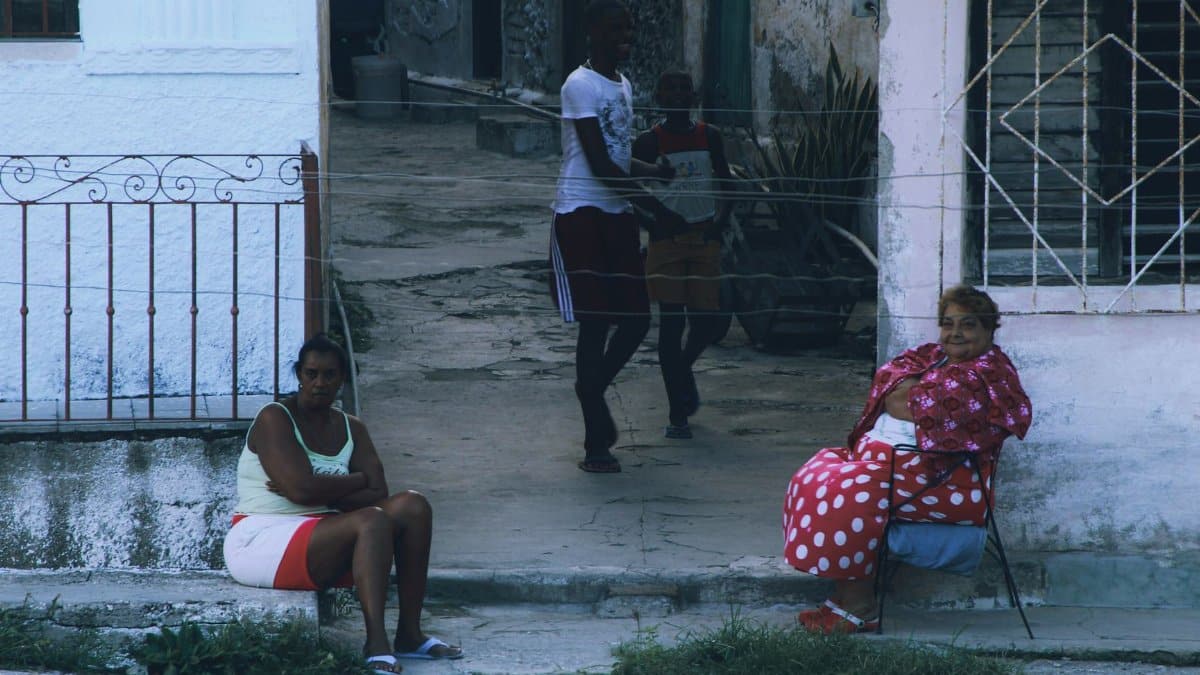 Two women sitting on a street corner in a residential area, conveying a sense of community life.