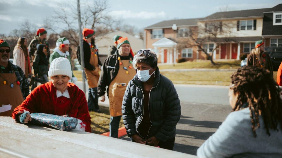 A neighborhood holiday gathering featuring adults dressed in elf costumes distributing gifts on a street.