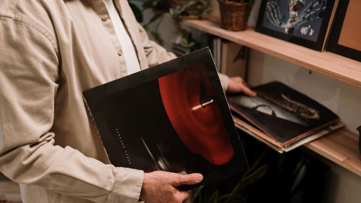 Adult holding vintage vinyl record, browsing a collection on a shelf indoors.