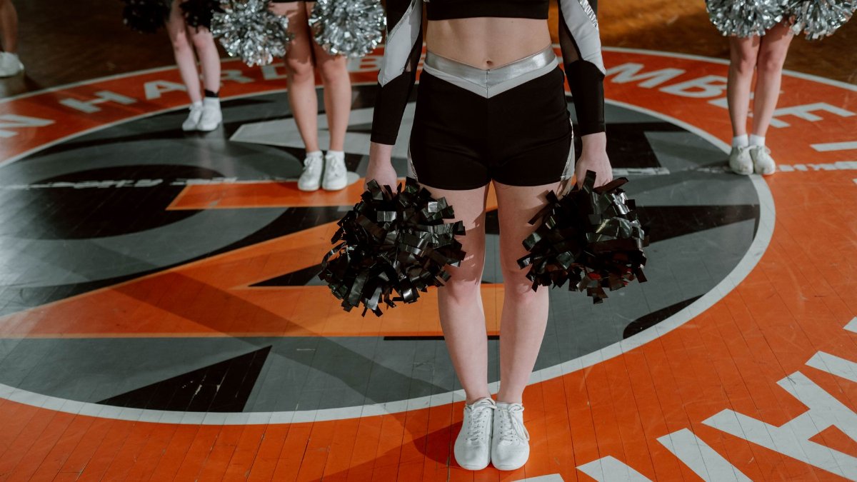 Cheerleading team in formation with pom-poms on an indoor basketball court, ready for performance.