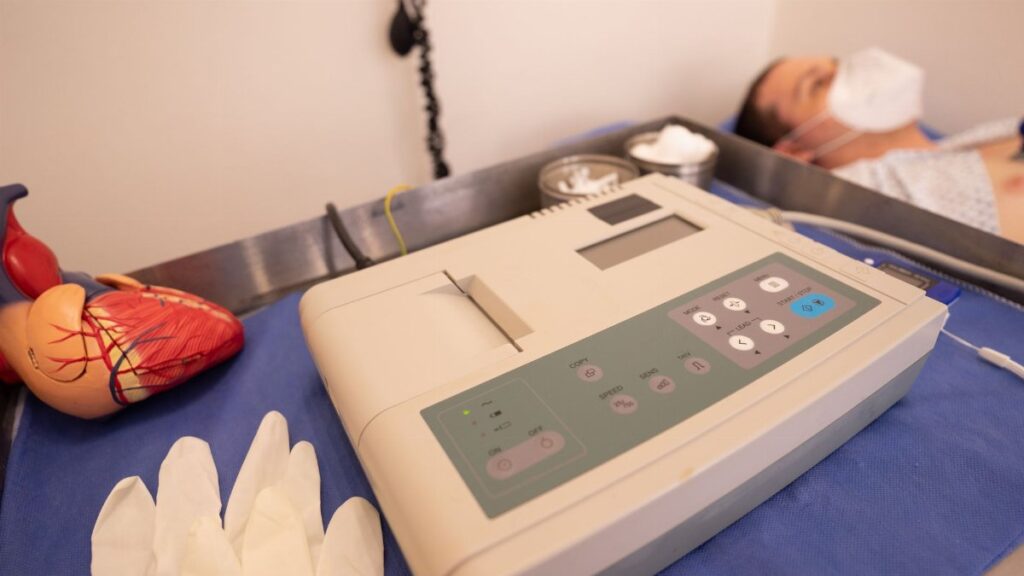 Close-up of ECG machine and model heart in a hospital setting.