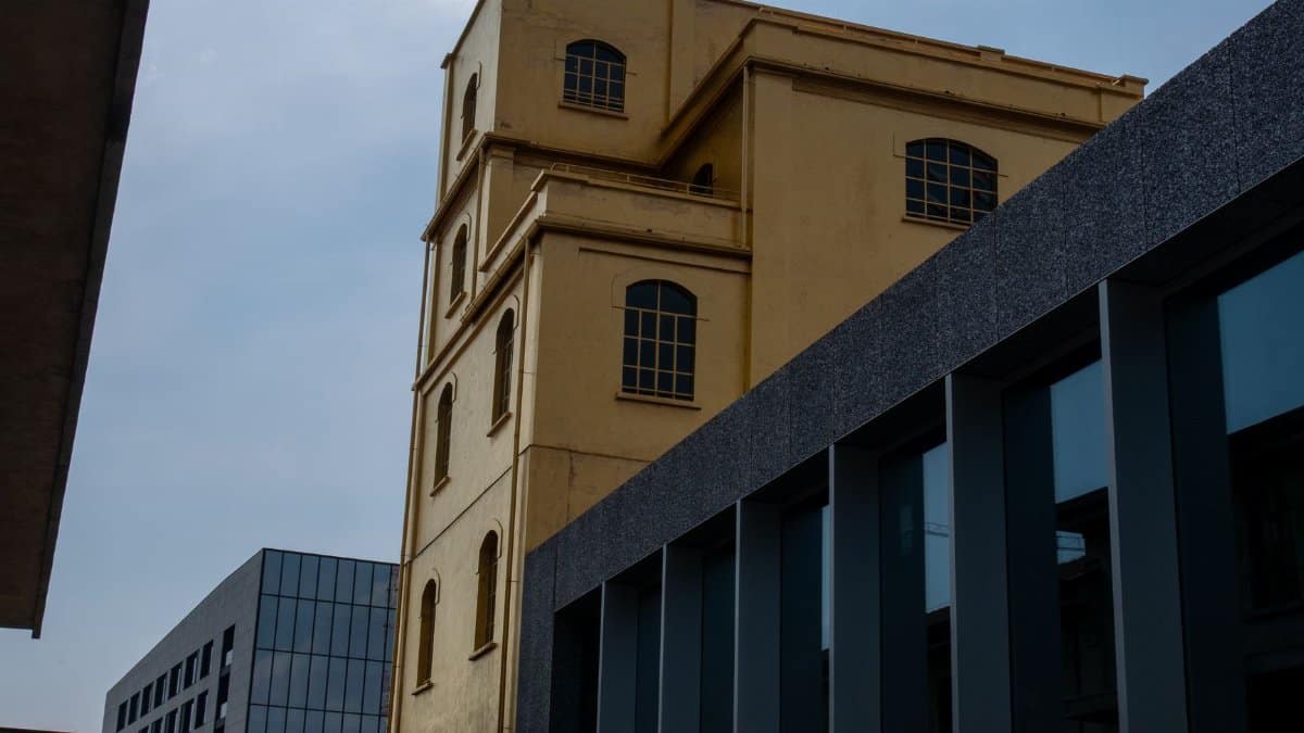 An old yellow building contrasts sharply with modern blue-gray architecture under a bright sky.