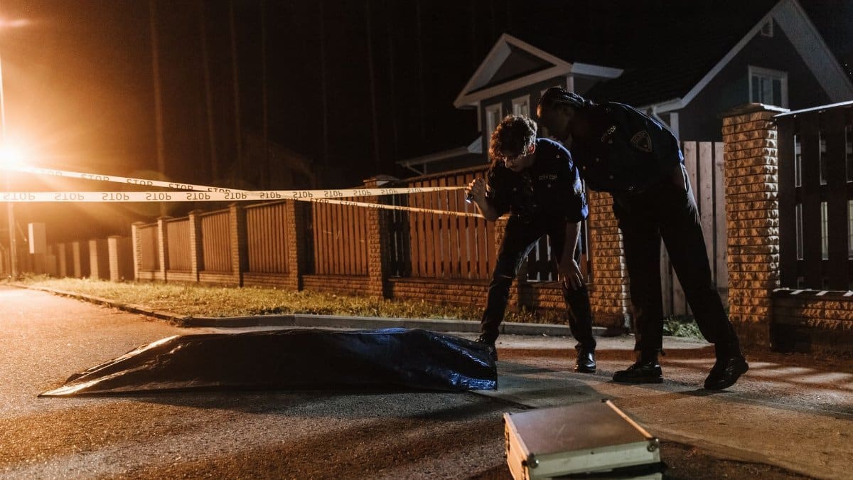 Police officers investigate a crime scene at night, examining evidence near a residential area.