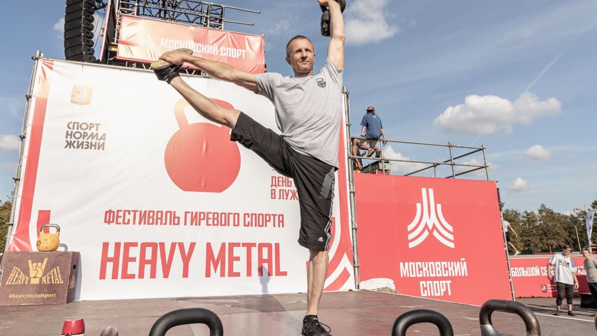 Man displaying strength at a kettlebell competition outdoor festival.