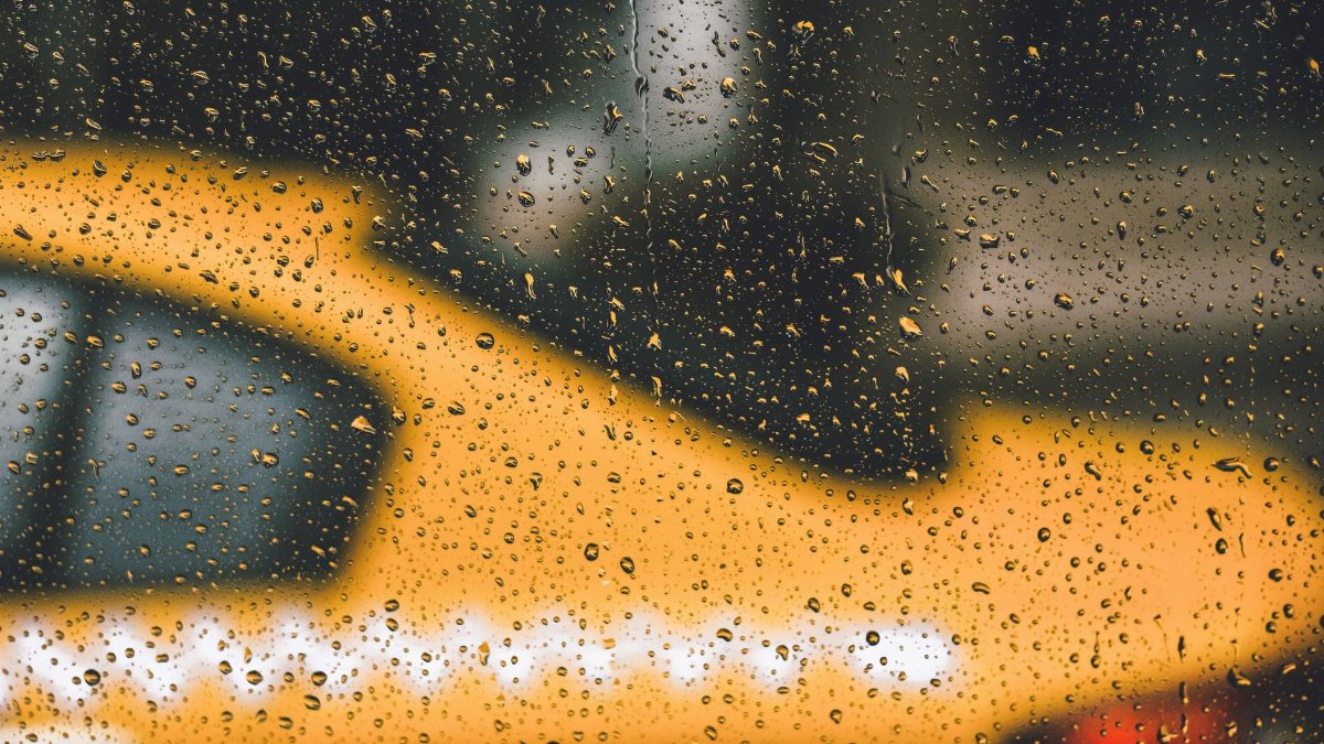 Blurry yellow taxi seen through rain-covered window in city, creating a moody urban vibe.